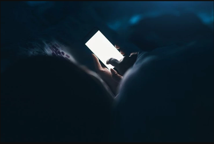 Persona acostada en la cama en la oscuridad usando un teléfono celular